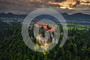Bled, Slovenia - Aerial drone view of beautiful illuminated Bled Castle Blejski Grad with dark rain clouds, golden sunset