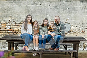 Blended family of five with two girls and a baby boy sitting on a table by an urban old brick wall