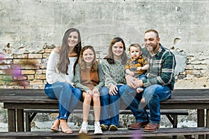 Blended family of five with two girls and a baby boy sitting on a table by an urban old brick wall