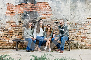 Blended family of five with two girls and a baby boy sitting on a table by an urban old brick wall
