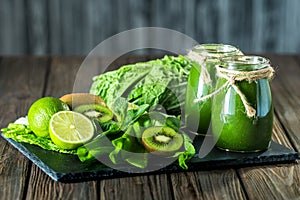 Blended green smoothie with ingredients on the stone board, wooden table