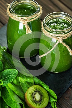 Blended green smoothie with ingredients on the stone board, wooden table