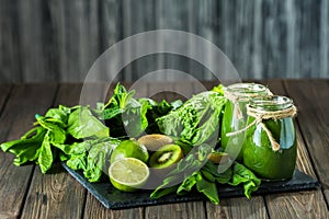 Blended green smoothie with ingredients on the stone board, wooden table