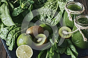 Blended green smoothie with ingredients on the stone board, wooden table