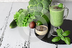 Blended green smoothie with ingredients on wooden table