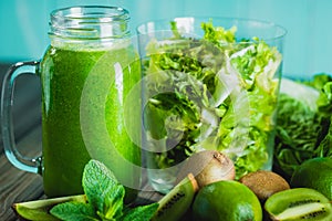 Blended green smoothie with ingredients on wooden table selectiv