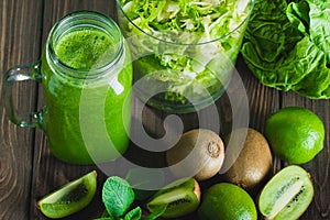 Blended green smoothie with ingredients on wooden table selectiv