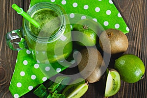 Blended green smoothie with ingredients on wooden table selectiv