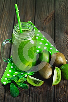 Blended green smoothie with ingredients on wooden table selectiv
