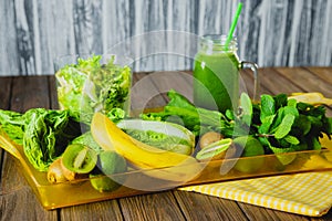 Blended green smoothie with ingredients on wooden table selective focus.