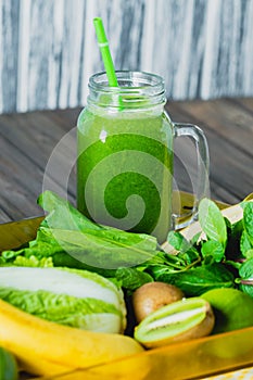 Blended green smoothie with ingredients on wooden table selective focus.