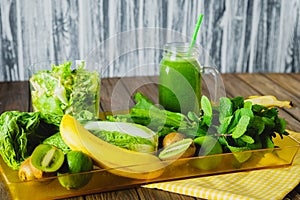 Blended green smoothie with ingredients on wooden table selective focus.