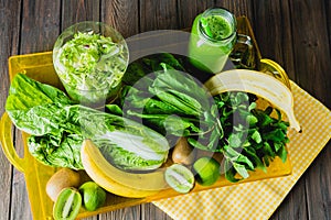 Blended green smoothie with ingredients on wooden table selective focus.