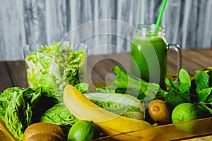 Blended green smoothie with ingredients on wooden table selective focus.