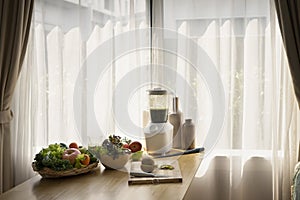Blender with fresh organic vegetables and fruits on wooden table in kitchen.