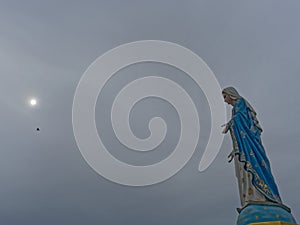 Blessed Virgin Mary, mother of Jesus, statue over dark sky background with the sun