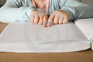 Blind child reading book written in Braille at wooden table, closeup. photo