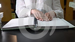 Blind girl reading a text of Braille in library. Hand touches the description in Braille.