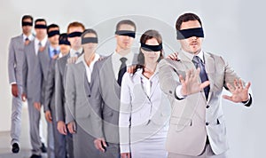 Blind leadership. A row of blindfolded businesspeople following a blindfolded leader.
