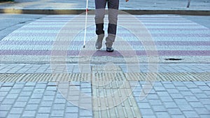 Blind male crossing street with white cane, using tactile tiles to navigate city