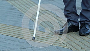 Blind male with white cane moving city on tactile pavement, infrastructure