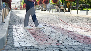 A blind man with a cane crosses the road. Young blind man with using safety stick for walking alone outdoors