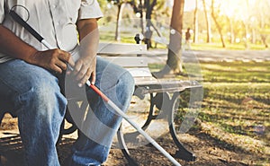 Blind man sits alone in a park holding a walking stick for the blind.