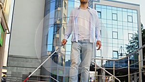 A blind man walking in city and using cane on pavement