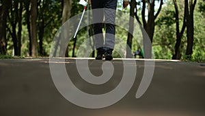 Blind man walking in park, using long cane to scan way for obstacle, orientation