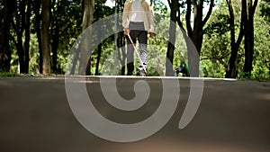 Blind man walking in park, using long cane to scan way for obstacle, orientation