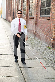 Blind man walking on sidewalk holding stick photo