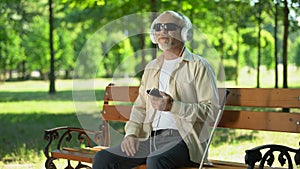 Blind old man wearing earphones listening audiobook, voice message in cellphone