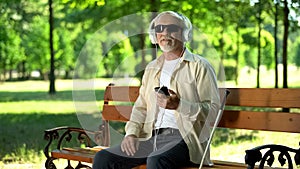 Blind old man wearing earphones listening audiobook, voice message in cellphone photo