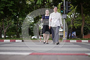 Blind person Asian woman with white cane crossing street walking on crosswalk with the sighted guide person senior woman by