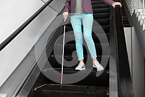 Blind person with long cane on escalator