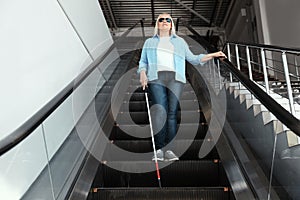 Blind person with long cane on escalator