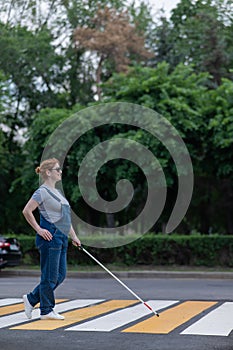 Blind pregnant woman crosses the road at a crosswalk with a cane.