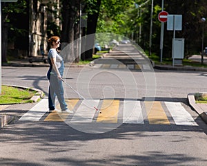 Blind pregnant woman crosses the road at a crosswalk with a cane.