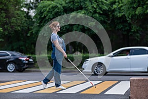 Blind pregnant woman crosses the road at a crosswalk with a cane.