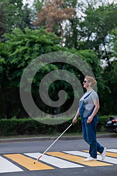 Blind pregnant woman crosses the road at a crosswalk with a cane.