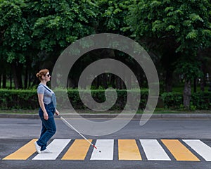 Blind pregnant woman crosses the road at a crosswalk with a cane.