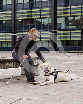 Blind or visually impaired woman resting with a guide dog on the bench