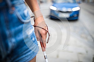 Blind woman walking on city streets, using her white cane