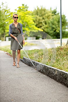 Blind woman walking on city streets, using her white cane