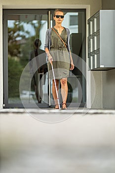 Blind woman walking on city streets, using her white cane