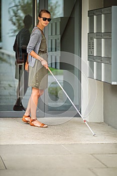 Blind woman walking on city streets, using her white cane