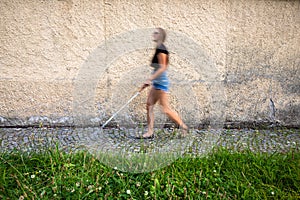 Blind woman walking on city streets, using her white cane