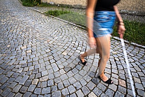 Blind woman walking on city streets, using her white cane