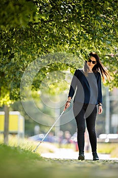 Blind woman walking on city streets, using her white cane