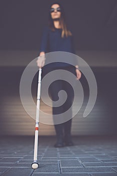 Blind woman walking on city streets, using her white cane